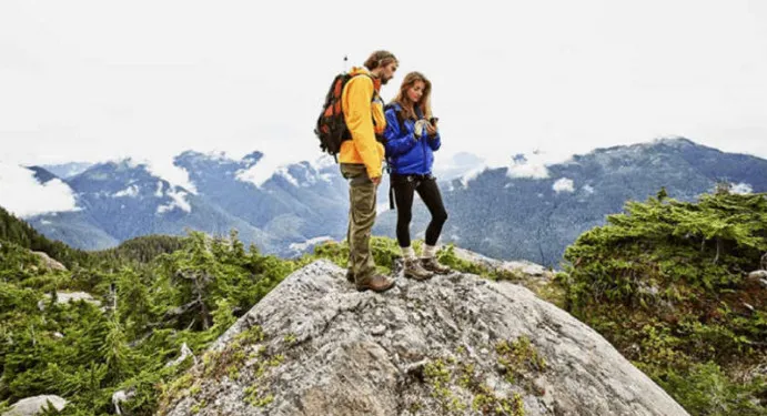 two people on a mountain top looking at a hand-held mobile device